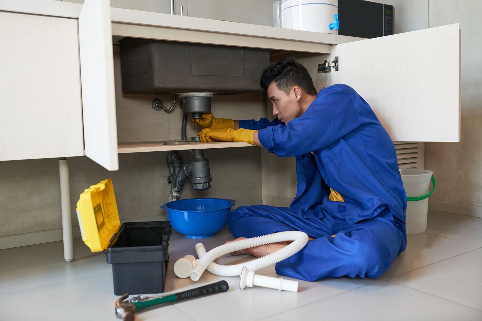 Plumber repairing pipes under a sink in a California home